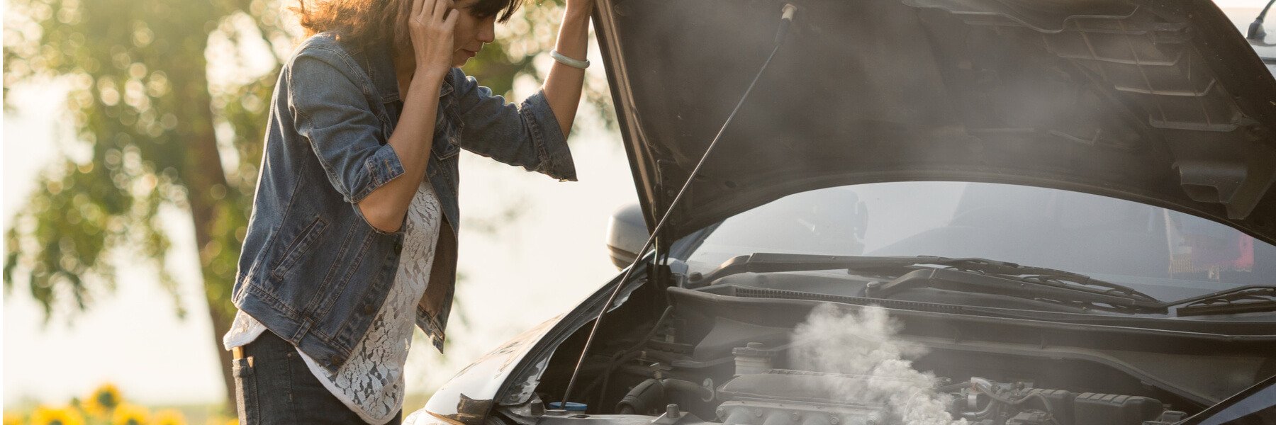 woman standing on the road by the broken car with smoke coming out the engine.