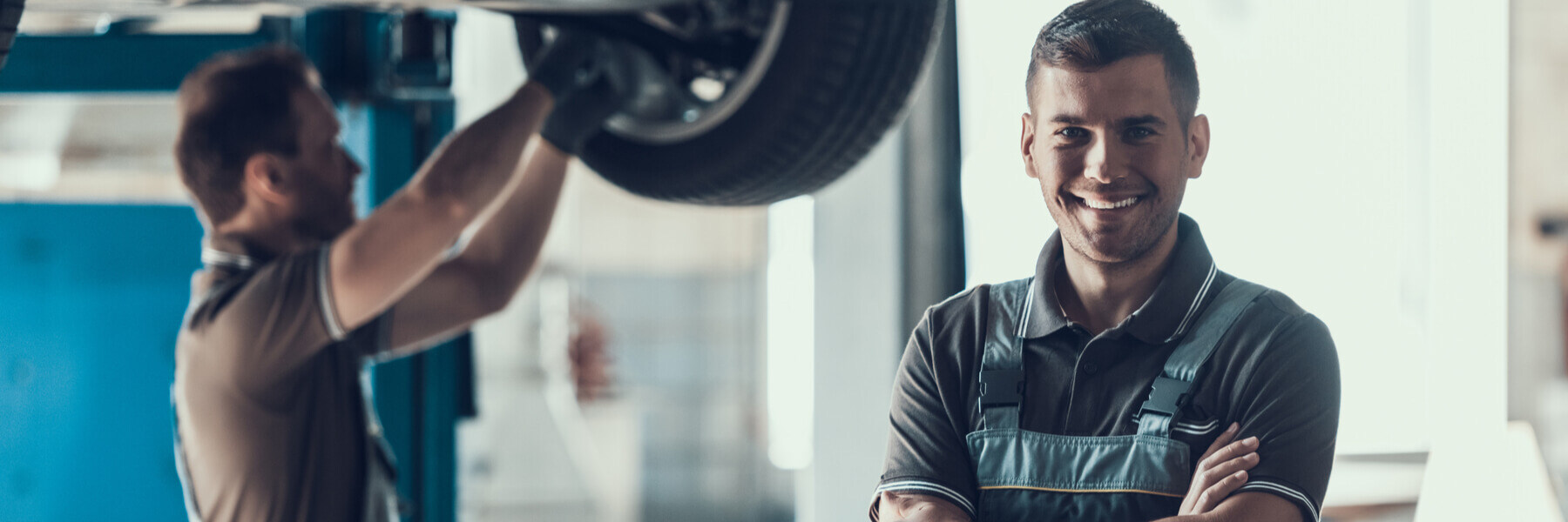 Happy local mechanic smiling, in background there is another mechanic working on a vehicle